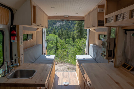 RV rental interior: a clean camper van with kitchen, benches, and an open back showcasing a stunning forest view.