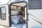 A happy black and gray dog sits on a bed inside a compact RV rental, ready for adventure. Ideal for pet travel.
