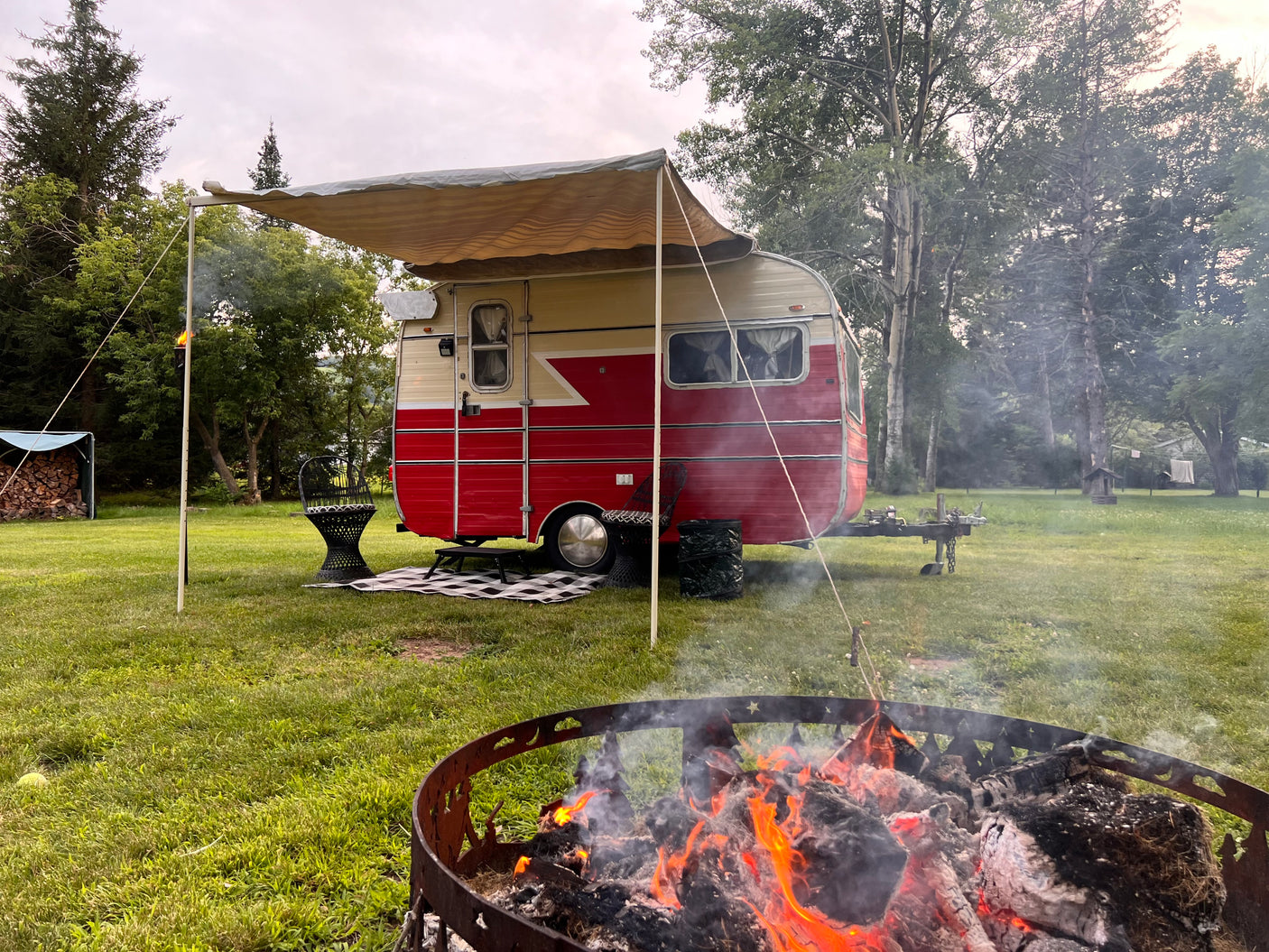 Relax at a vintage RV rental campsite! A cozy fire pit burns brightly, and an awning provides shade for this classic camper.