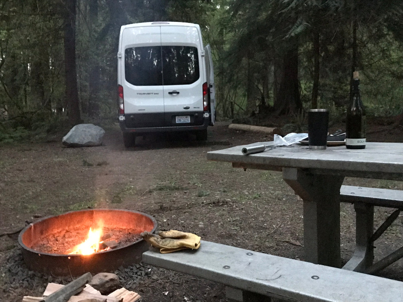 RV rental campsite nestled in the woods with a cozy campfire and picnic table, perfect for outdoor adventure.