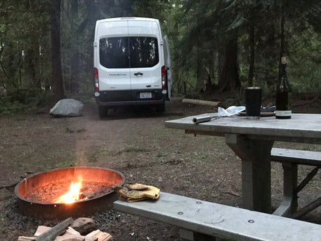RV rental campsite nestled in the woods with a cozy campfire and picnic table, perfect for outdoor adventure.