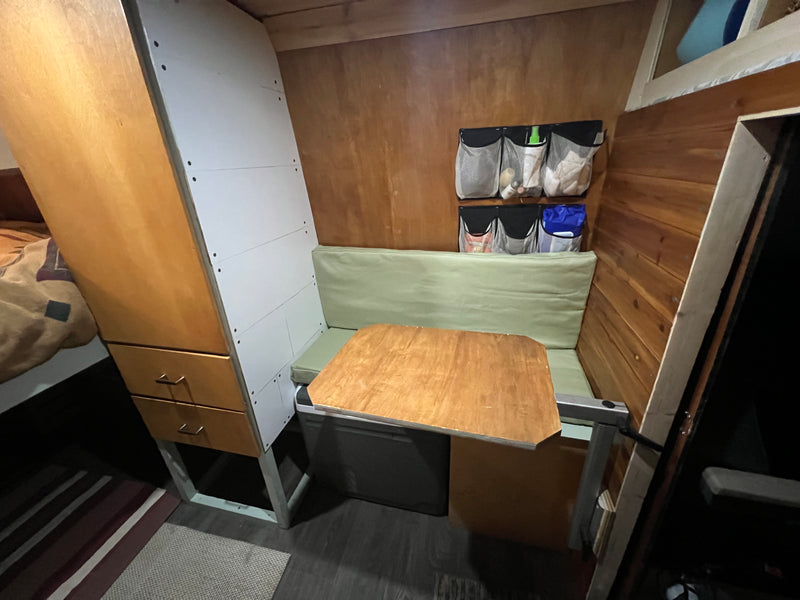 RV rental interior featuring a cozy dining area with green cushions, wooden table, smart storage, and wood paneling. — photo 6