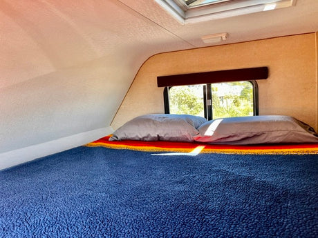 Cozy rv rental bed with pillows and window view. This comfortable camper sleeping area includes a skylight.