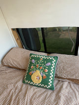 Cozy RV rental interior with brown gingham bedding and a green, floral embroidered pillow by the window.