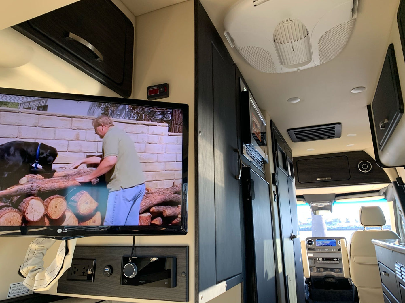 RV rental interior: A TV and audio system for entertainment, with clean modern cabinets and a view into the driver's cabin.