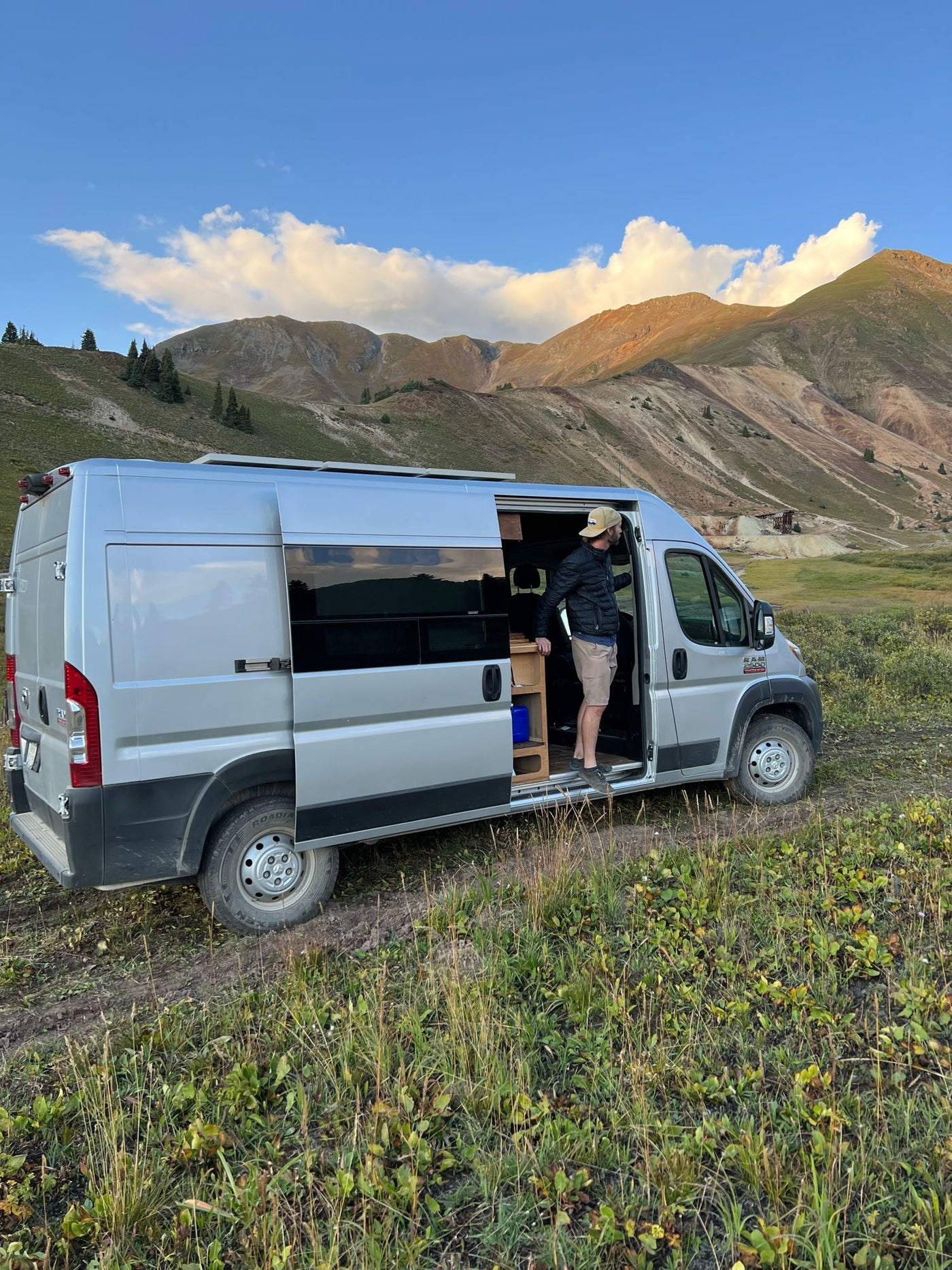  parked on a dirt path in grassy mountains.|Custom wood-built RV rental camper van. See exterior — photo 2