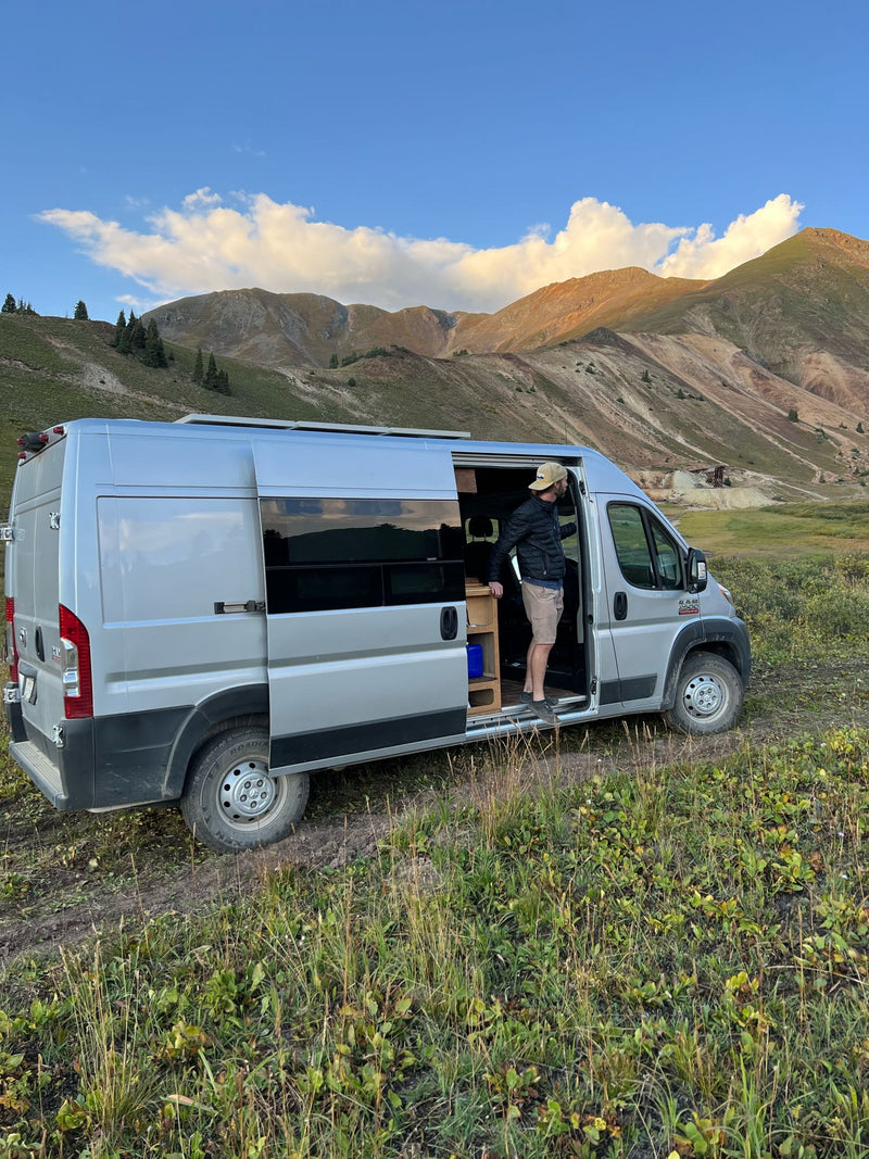  parked on a dirt path in grassy mountains.|Custom wood-built RV rental camper van. See exterior — photo 2