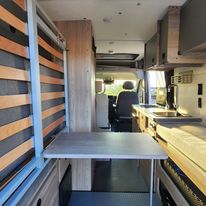 Inside this RV rental: compact kitchen, bed, and dining area with a slatted bed structure. Ready for adventure!