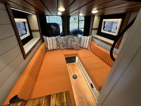 Cozy rv rental interior featuring a spacious U-shaped lounge with vibrant orange cushions, wood accents, and scenic windows.