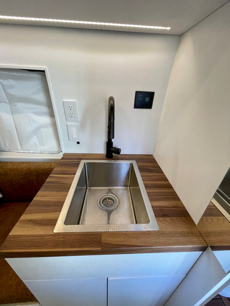 Modern RV rental kitchen with a stainless steel sink, black faucet, wood countertop, and smart control panel.