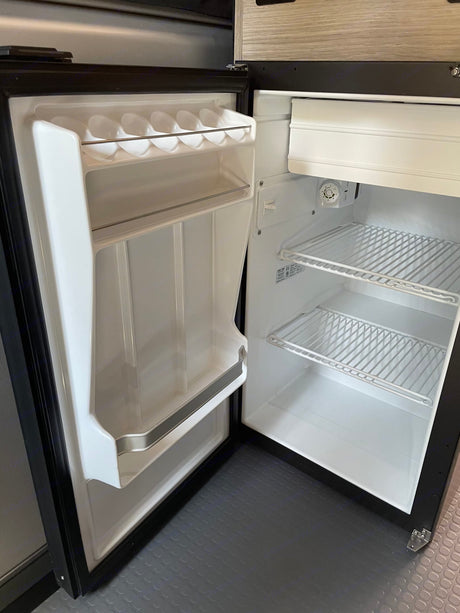Empty, clean mini-fridge within an rv rental. Features wire shelves, a freezer, and door storage, ready for your trip's food.
