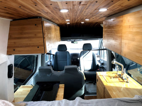 Explore this stylish camper van RV rental interior: wooden ceiling, kitchen with stove & sink, and front seating.
