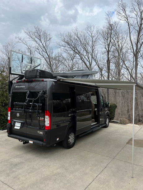 Black rv rental camper van with extended awning, roof-top tent, bike rack, and a unique basketball backboard attachment.