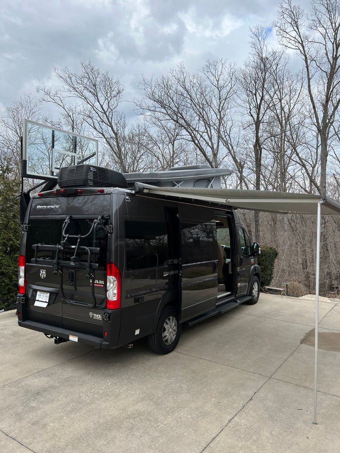 Black rv rental camper van with extended awning, roof-top tent, bike rack, and a unique basketball backboard attachment.