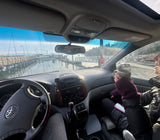 From our vehicle, enjoying a marina view with sailboats, coffee in hand. Planning our RV rental adventure, outside temp 34. Scenic travel.