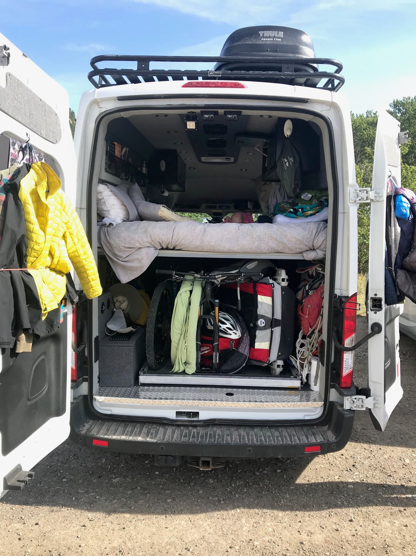 RV rental van with open back, showing packed interior: bikes, gear, and bedding. Thule cargo box on roof.