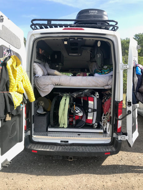 RV rental van with open back, showing packed interior: bikes, gear, and bedding. Thule cargo box on roof.