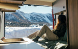 Inside a cozy RV rental, a person enjoys vast snowy mountain views. Ideal for a winter travel adventure.