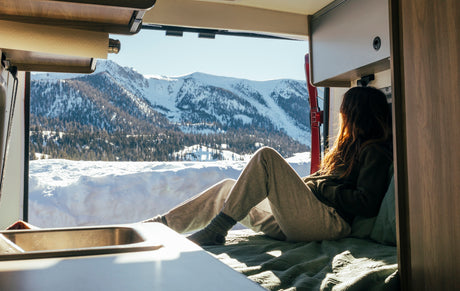 Inside a cozy RV rental, a person enjoys vast snowy mountain views. Ideal for a winter travel adventure.