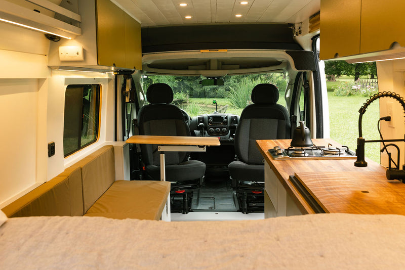 Inside an RV rental: a modern camper van interior showing the kitchenette, bench seating, and driver's cabin beyond. — photo 6
