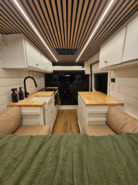 Cozy and modern RV rental interior featuring a slatted wood ceiling with LED lights, a full kitchenette, and comfortable bench seating.