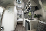 Modern RV rental interior: kitchen with microwave, fridge, sink; cozy bedroom; sleek metallic and light wood paneling throughout.