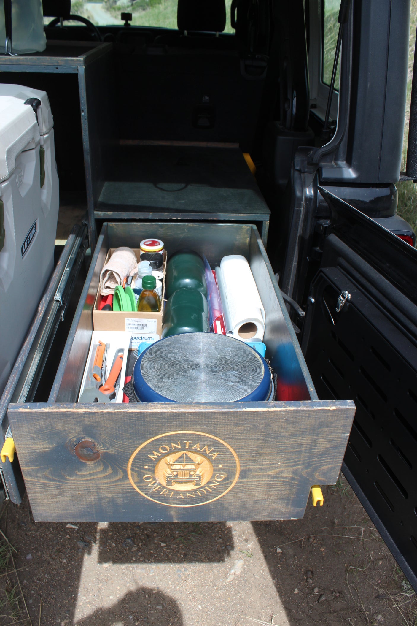 Custom rv rental overlanding setup: a pull-out kitchen drawer packed with camping cooking gear, including a pan, spices, and paper towels.
