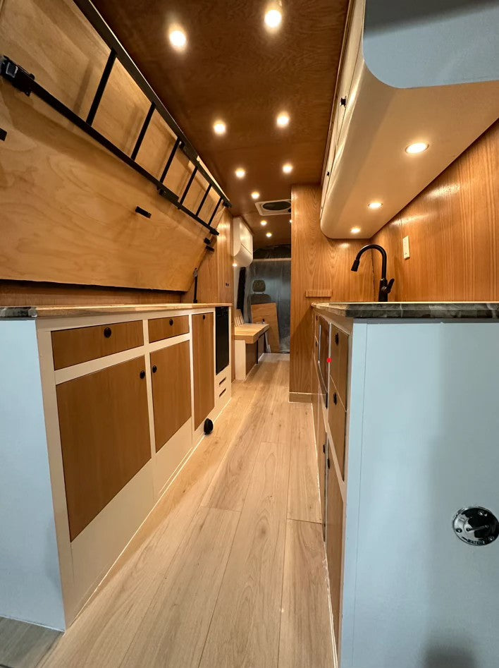 Tour this custom RV rental camper van interior. Light wood, kitchen with faucet, bunk bed, and ample storage.