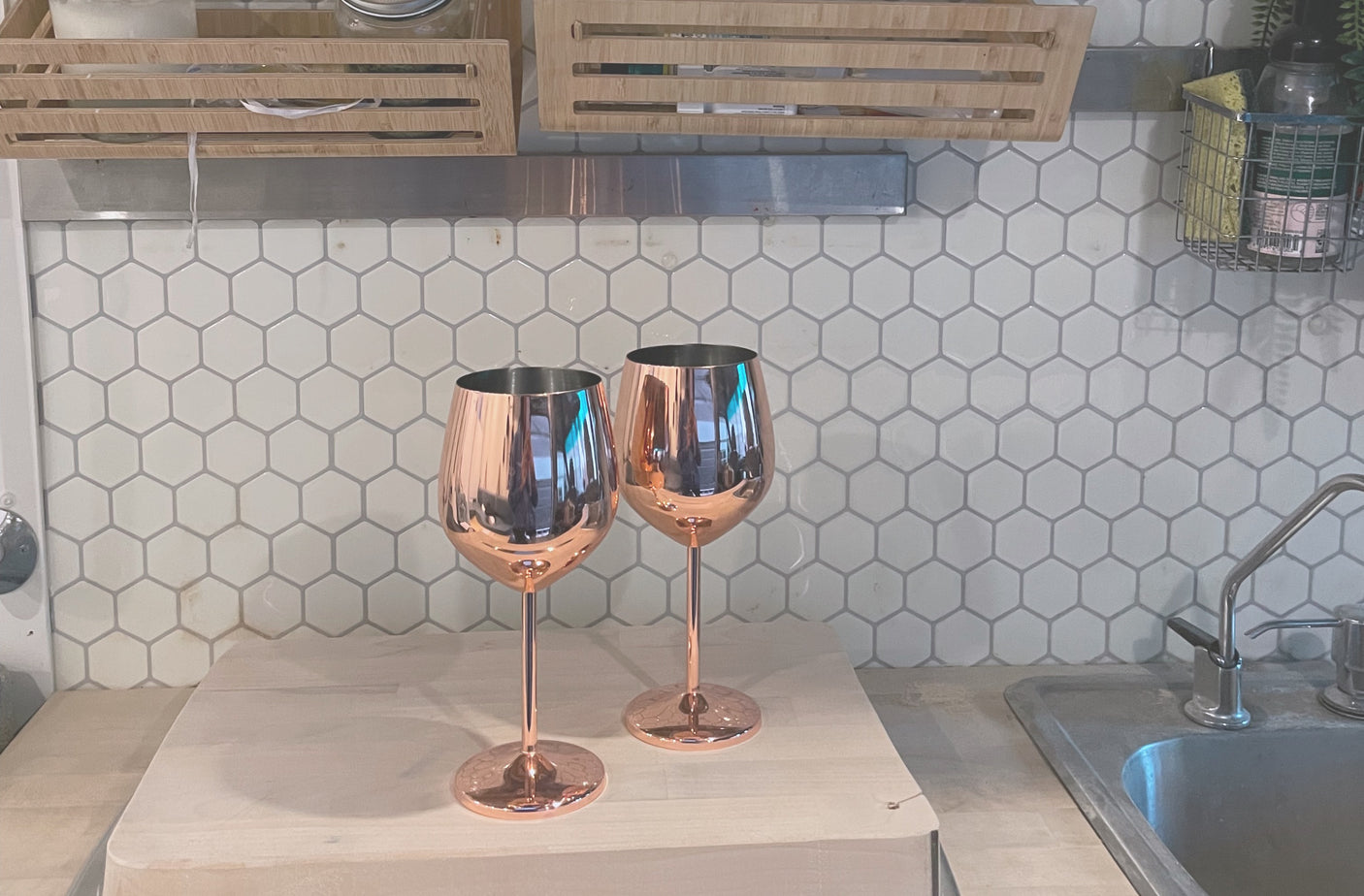 Stylish RV rental kitchen with copper wine glasses, hexagonal backsplash, and compact sink area.