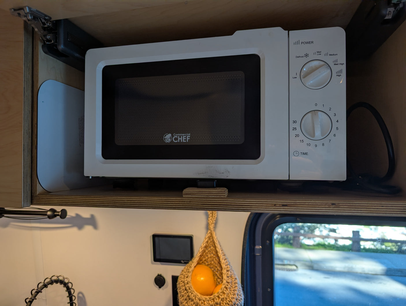 This RV rental kitchen features a compact Commercial CHEF microwave neatly tucked into an overhead cabinet for space-saving.