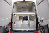 RV rental van conversion: open rear view showing elevated bed, storage boxes, and well-lit interior.