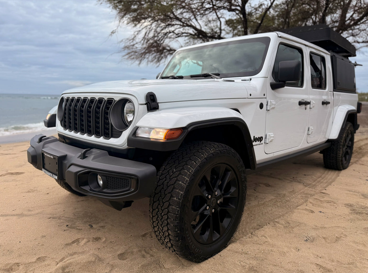 White Jeep Gladiator pickup with rooftop tent on a sandy beach by the ocean, perfect for your next RV rental adventure.