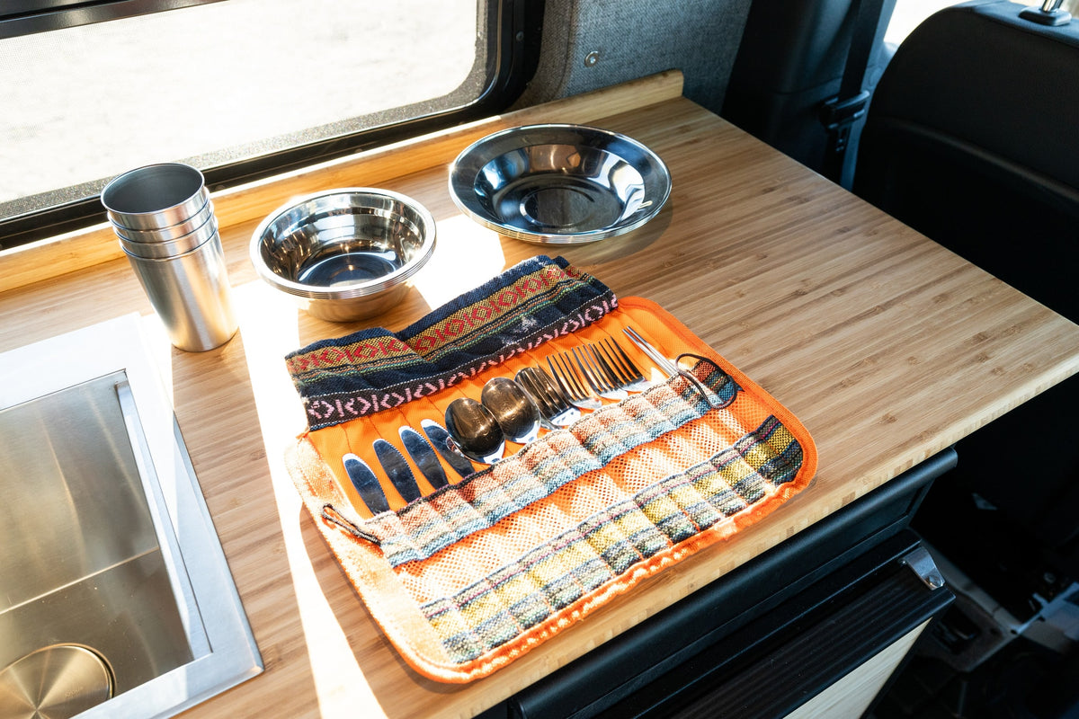 RV rental kitchen: bamboo counter, stainless steel sink, cups, bowls, and a patterned utensil roll with silverware. — photo 12