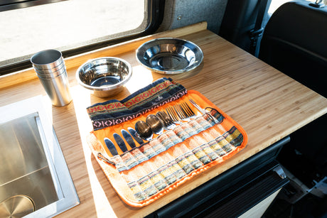 RV rental kitchen: bamboo counter, stainless steel sink, cups, bowls, and a patterned utensil roll with silverware.