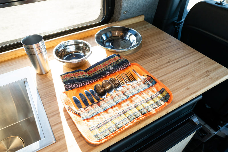 RV rental kitchen: bamboo counter, stainless steel sink, cups, bowls, and a patterned utensil roll with silverware. — photo 12