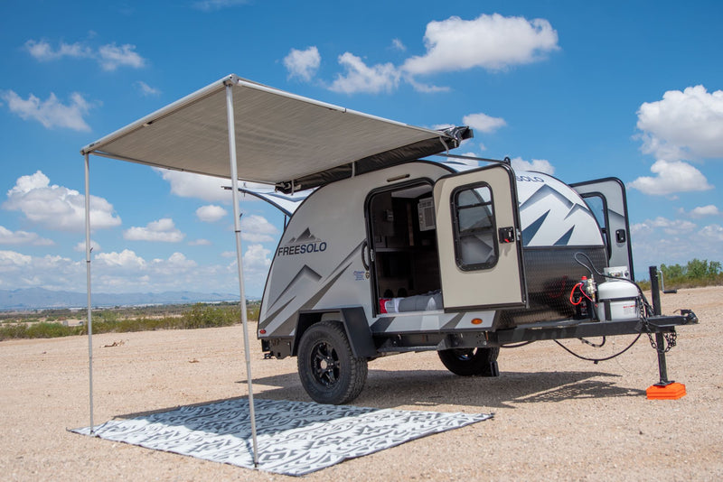 Compact Freesolo RV rental travel trailer set up for outdoor camping. Awning extended in a sunny desert scene.|This RV rental's outdoor kitchen is ready for adventure! Features a stove — photo 1