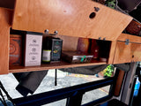 RV rental interior: Open wooden cabinet in a van, showing stored tea, avocado oil, and health supplements for travel convenience.