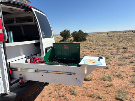 RV rental outdoor kitchen: A pull-out stove from a camper van cooking in an arid landscape with tortillas on a side table.
