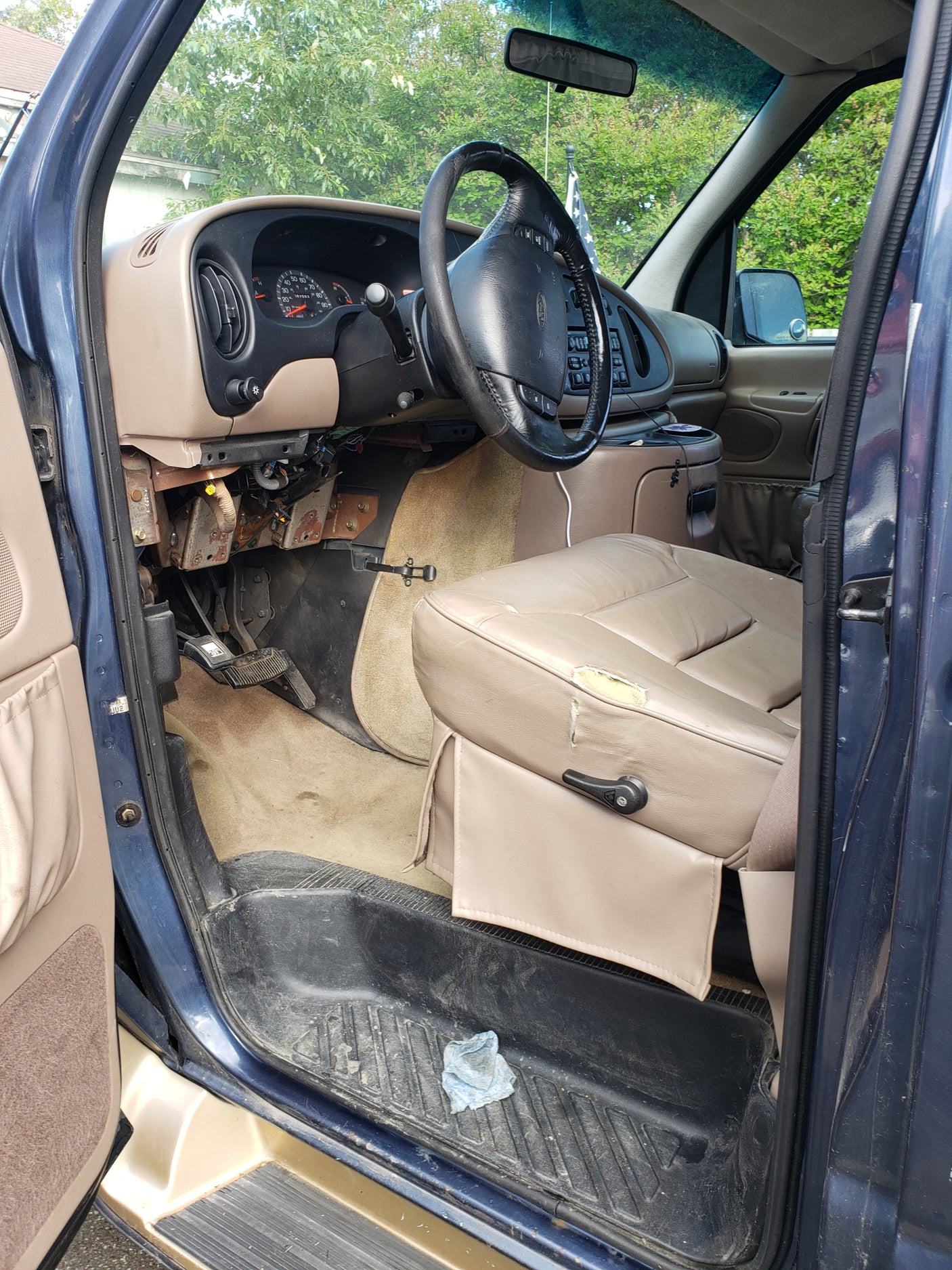 RV rental van interior: driver's seat (torn), exposed dash wiring, steering wheel, and dirty floor mats.