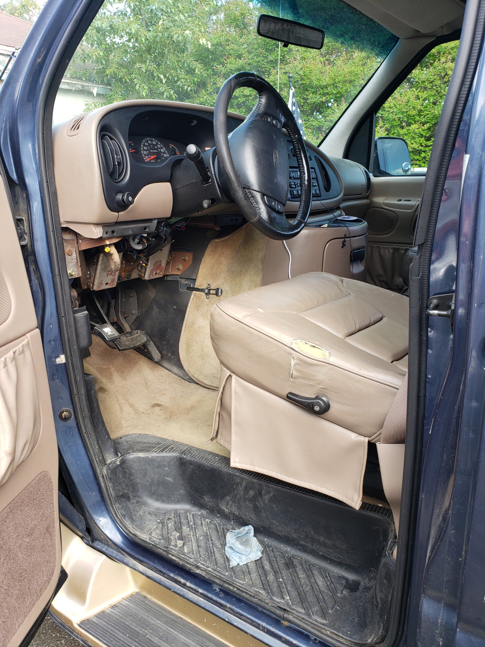RV rental van interior: driver's seat (torn), exposed dash wiring, steering wheel, and dirty floor mats.