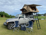 This overland RV rental features a silver Jeep Wrangler with a rooftop tent, chairs, and a cooler, ready for adventure.
