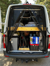 Rear view of an organized RV rental camper van, revealing a raised bed, bike, and essential gear for outdoor adventures.