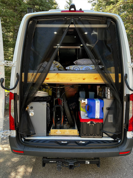 Rear view of an organized RV rental camper van, revealing a raised bed, bike, and essential gear for outdoor adventures.