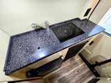 This RV rental's modern kitchenette features a speckled countertop, induction cooktop, sink, faucet, and mini-fridge.