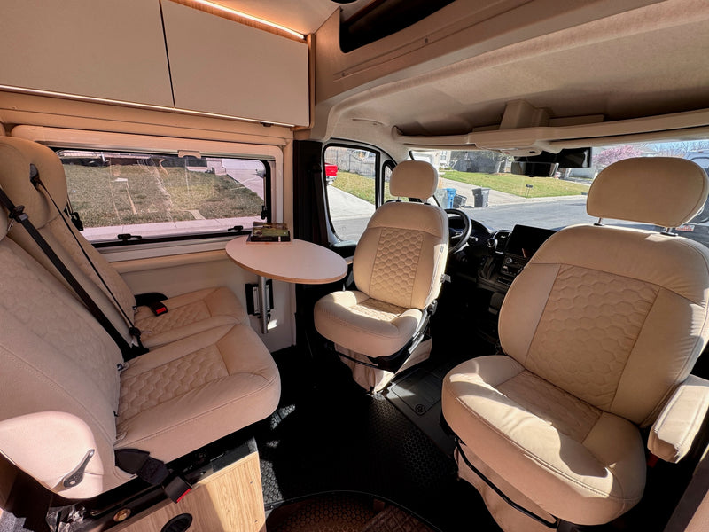 Step inside this comfortable RV rental. Features include light-colored swivel seats, a compact dinette, and overhead storage. — photo 9