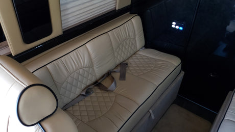 RV rental interior: luxurious beige leather bench seating with quilted patterns, seatbelts, and a lit control panel.