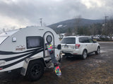 White Boondock Lite teardrop camper (RV rental) and Subaru Forester, with a snowboard, at a snowy mountain resort.