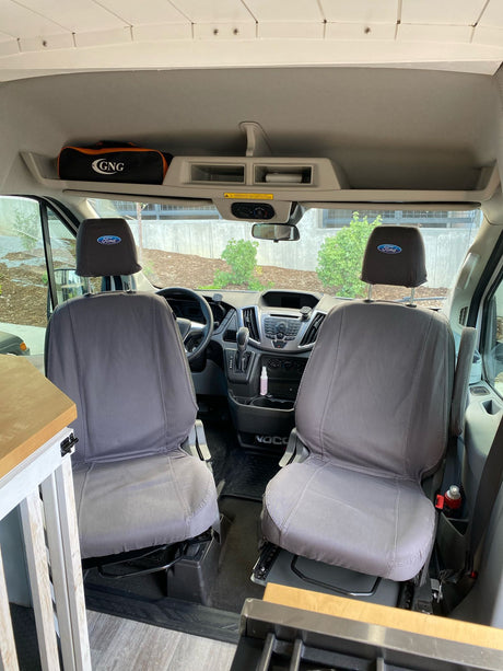 Front cabin of an RV rental, featuring swiveling Ford Transit seats, dashboard, and overhead storage, ideal for a camper van adventure.