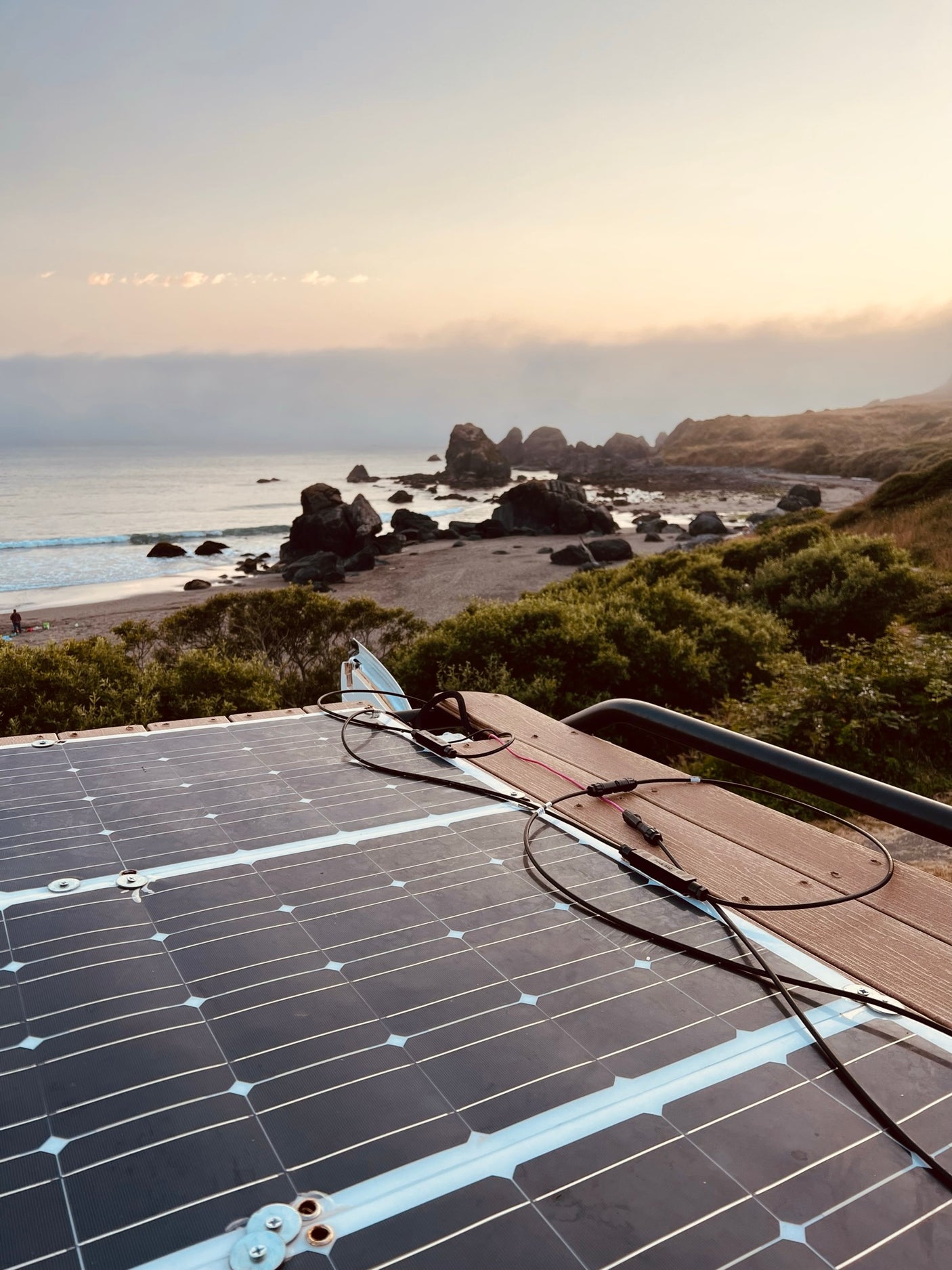 An rv rental's rooftop solar panels capture power overlooking a misty beach with sea stacks.