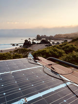 An rv rental's rooftop solar panels capture power overlooking a misty beach with sea stacks.